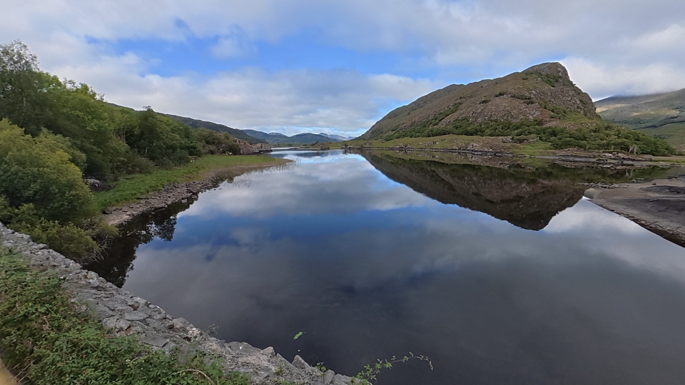 A calm lake reflecting a rocky mountain and blue sky