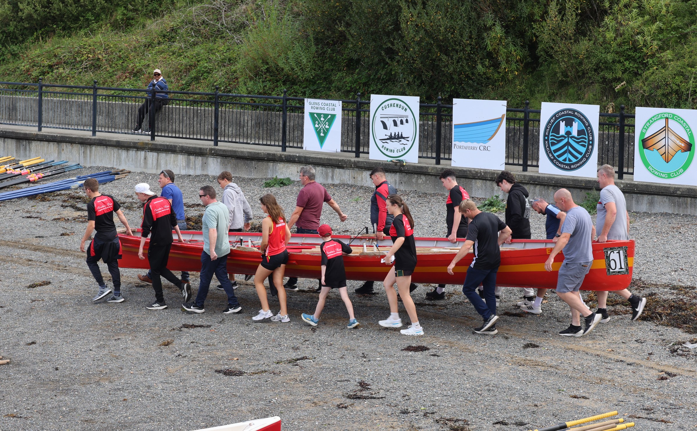 A crew carrying a red rowing boat towards the water
