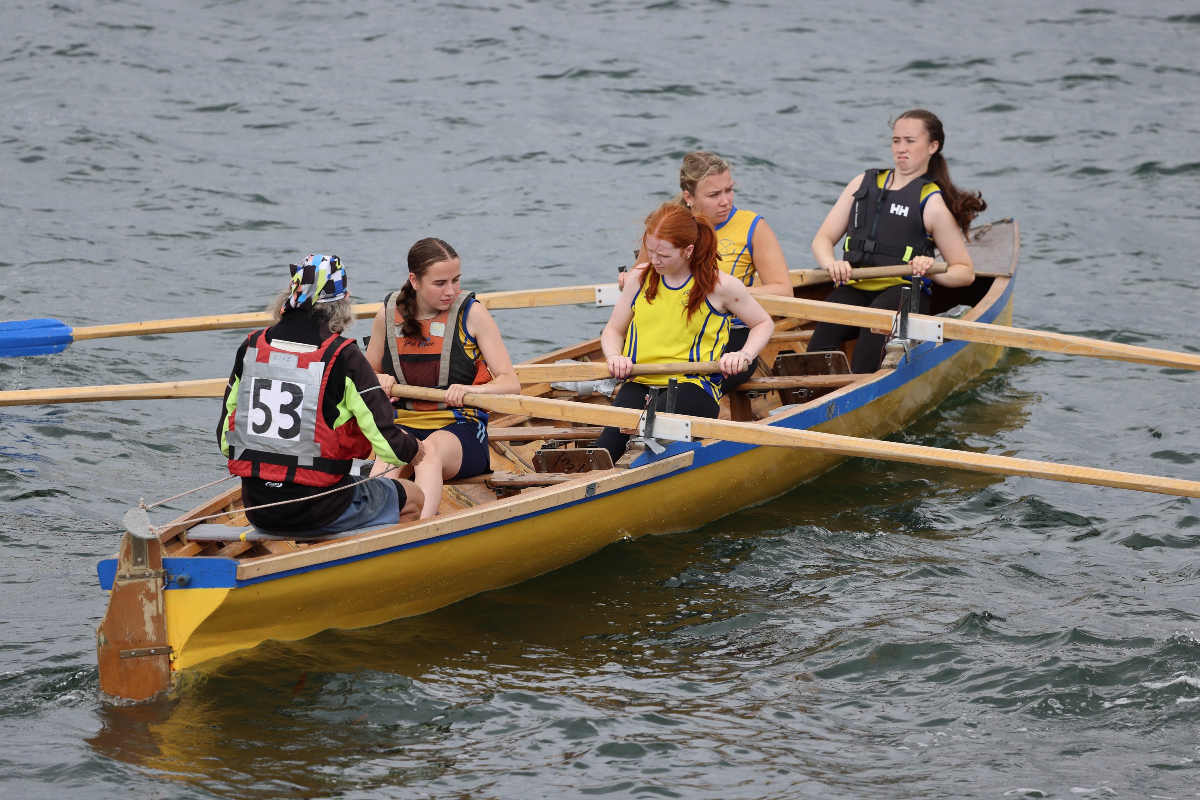 A crew in a yellow coastal rowing boat preparing to race