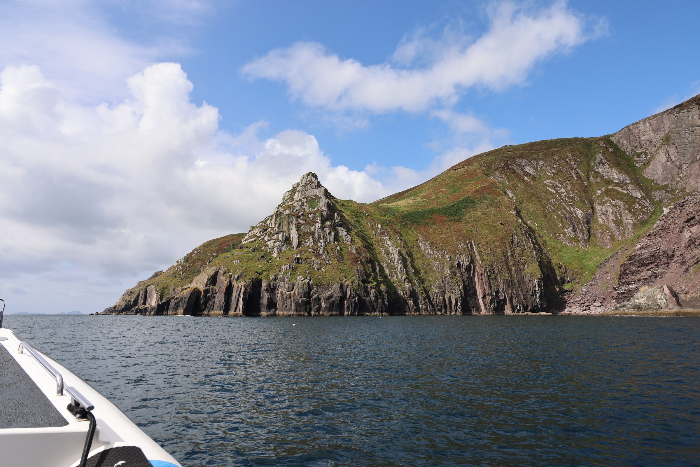 A steep green headland rising from layered sea cliffs