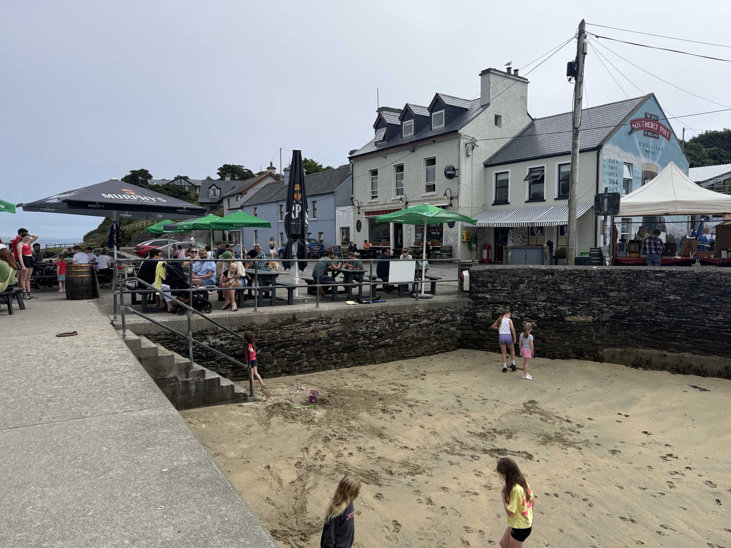 People sitting outside O'Sullivan's Bar beside the tiny harbour beach