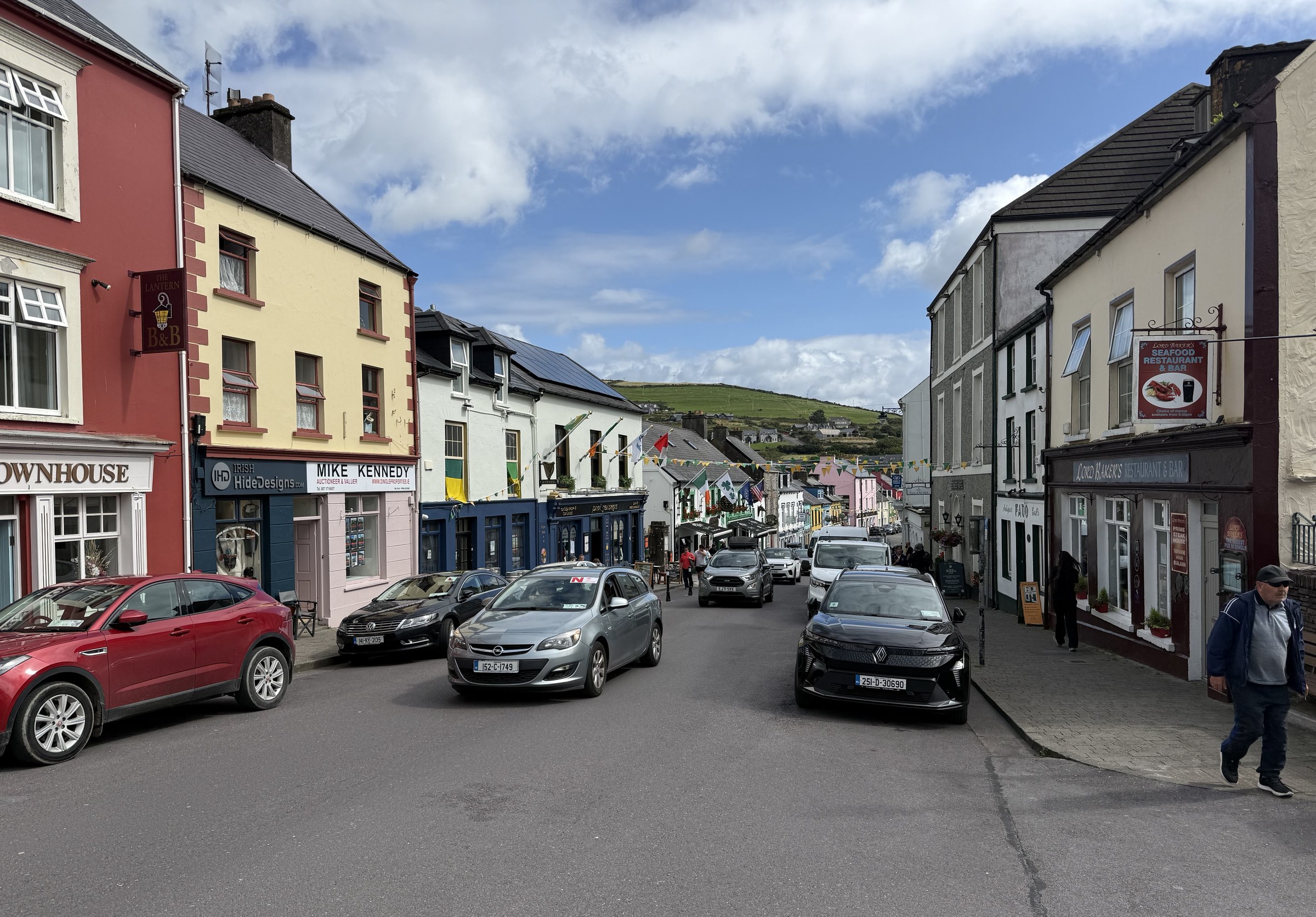 Cars and colourful shopfronts lining a busy street through central Dingle
