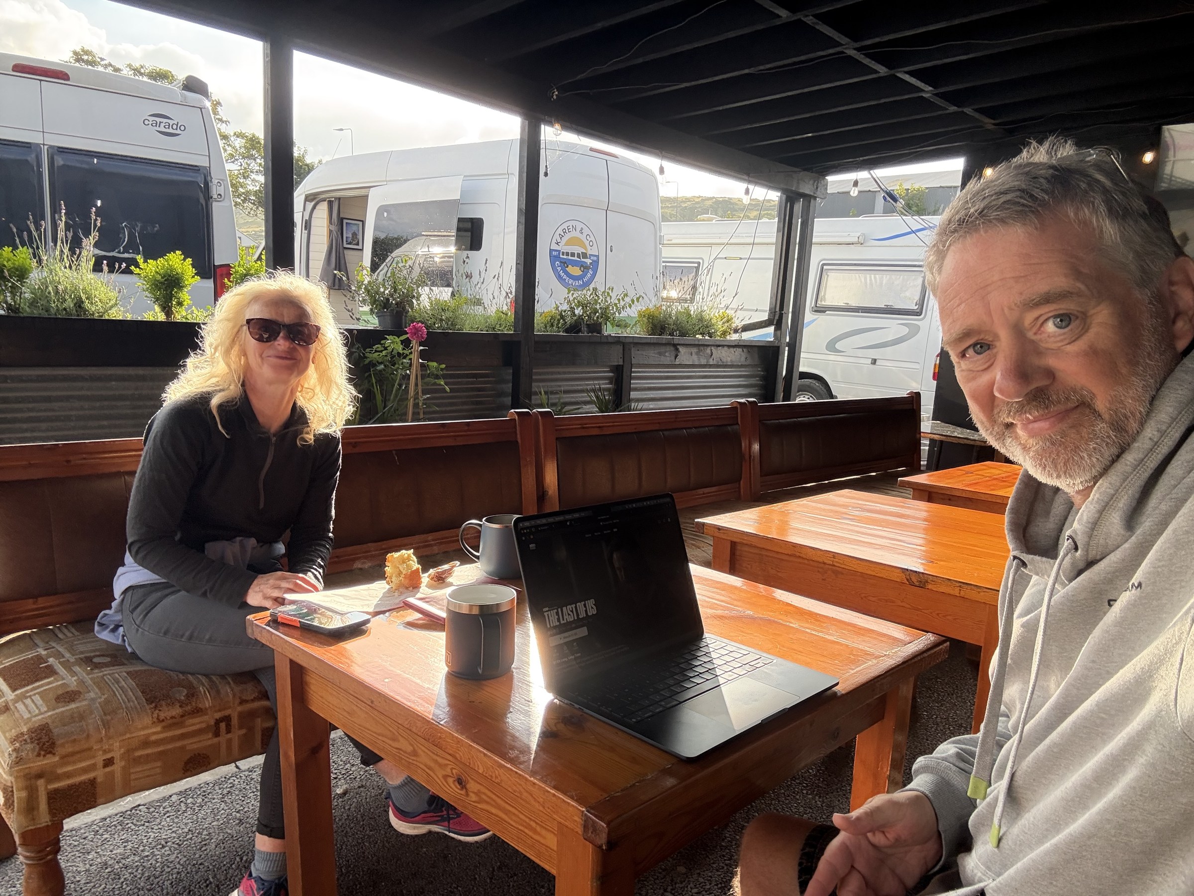 Sue and John drinking morning coffee in the covered seating area at Bridge House