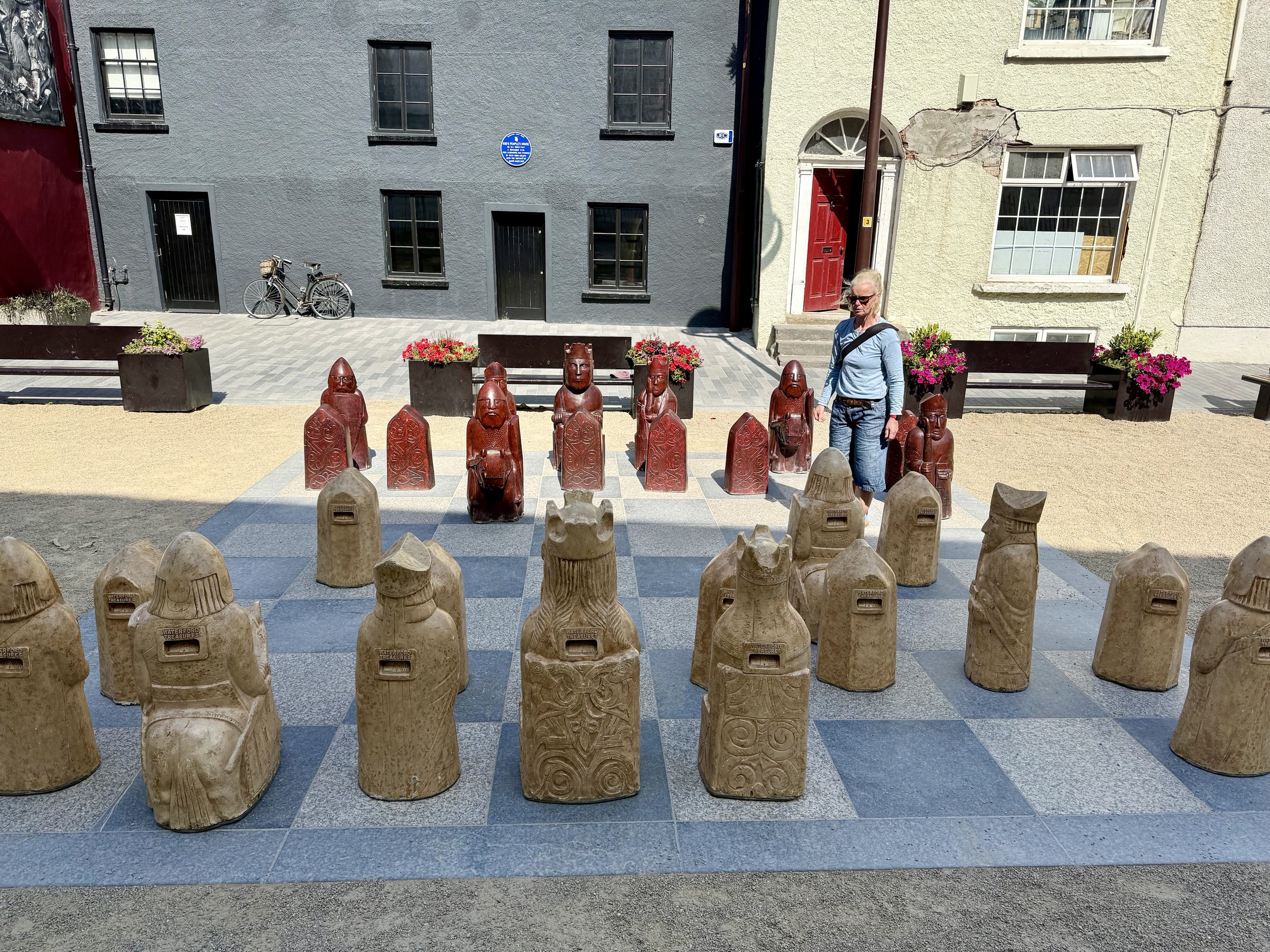Sue standing alone behind one side of an oversized outdoor chessboard