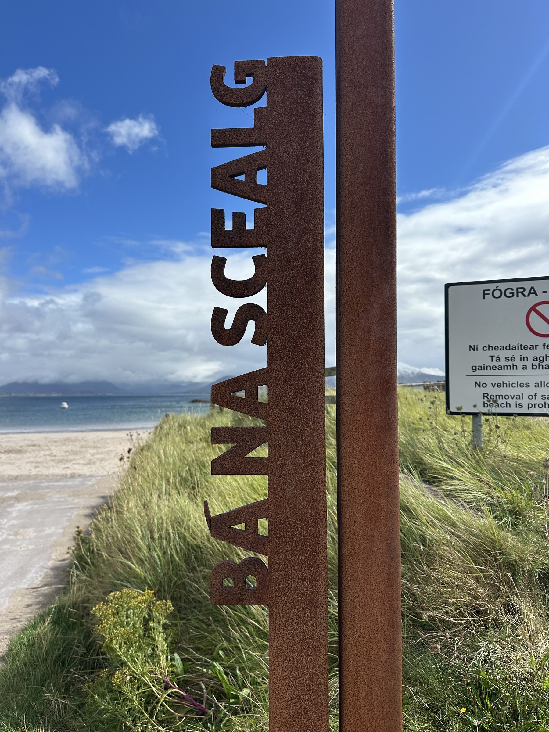 A rusted Ballinskelligs sign with the beach beyond