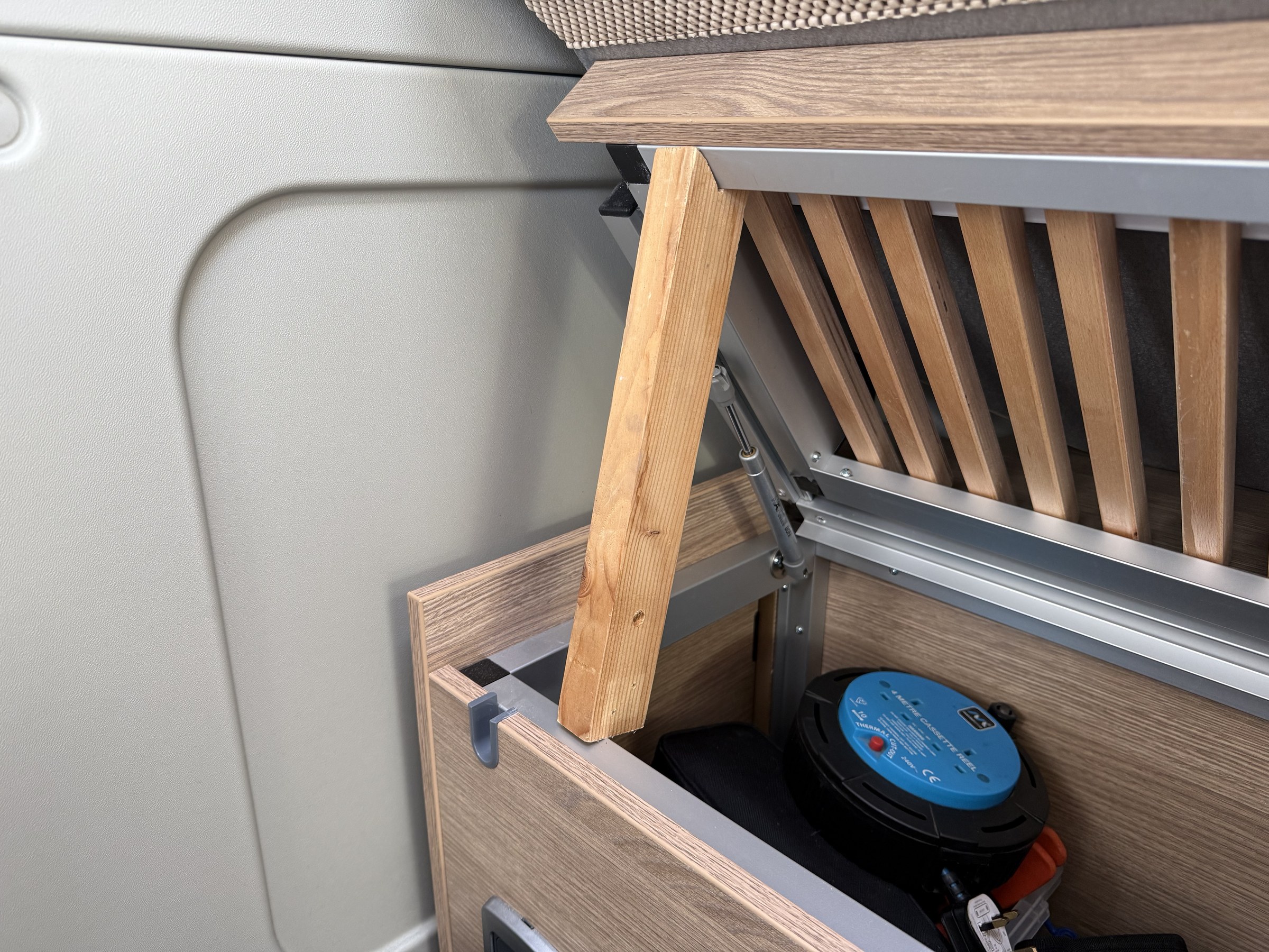 The wooden prop made to hold up an underbench storage lid