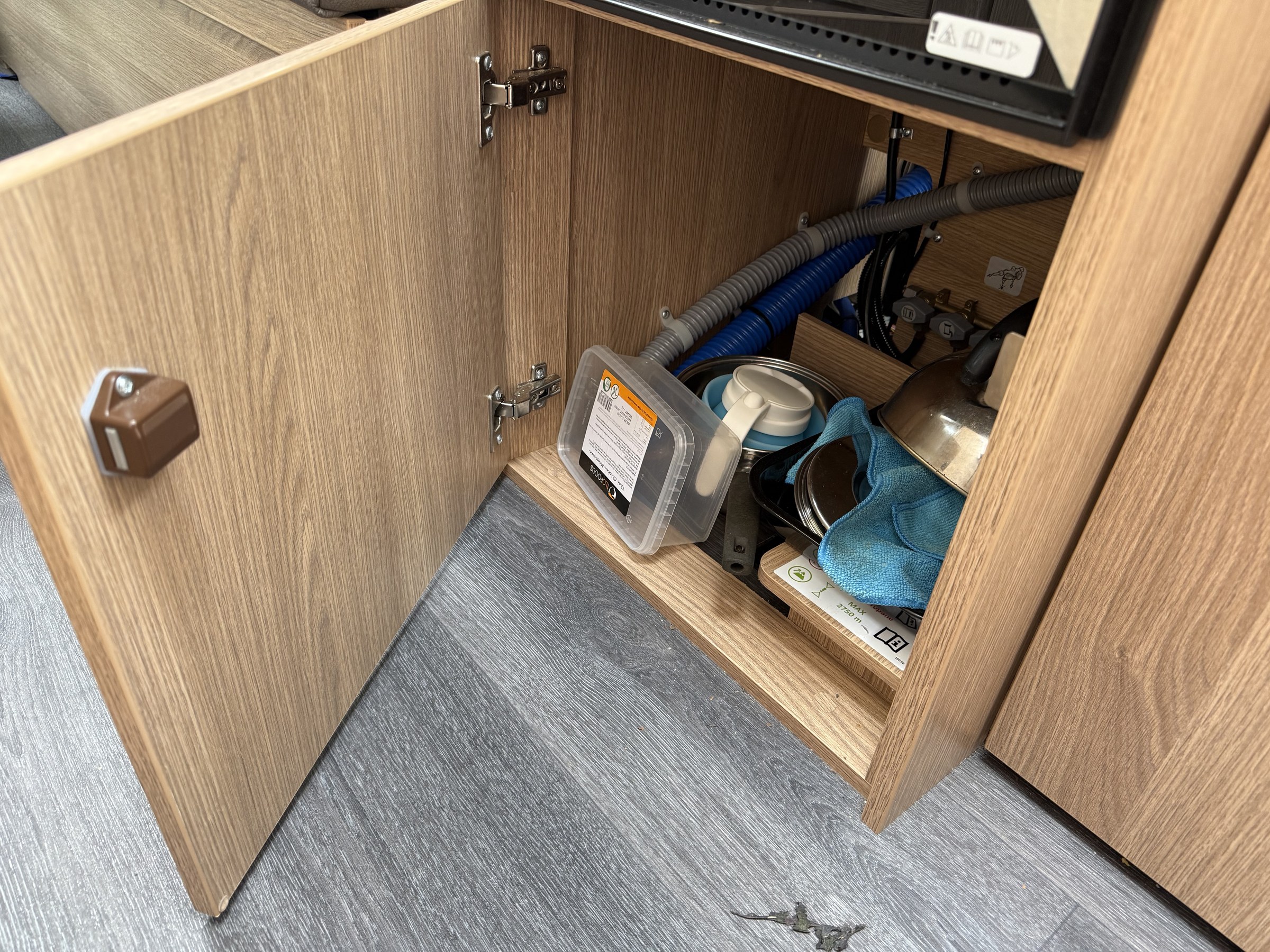 Pans, a kettle and other kitchen equipment packed into the cupboard below the oven